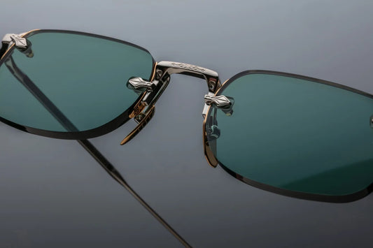 Rimless Jacques Marie Mage sunglasses with teal lenses and a combination of silver and gold hardware