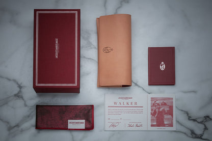Jacques Marie Mage signature burgundy packaging and accessories, featuring Italian-handcrafted leather case, microfiber cleaning cloth/pocket square, silk fabric-covered packaging, and letterhead press certificate with limited edition serial number and craftsmen signature. - Side Profile