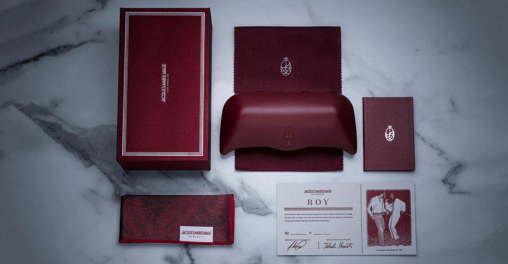 Jacques Marie Mage eyeglass accessories featuring the signature burgundy box, leather clamshell case, and numbered certificate of authenticity.